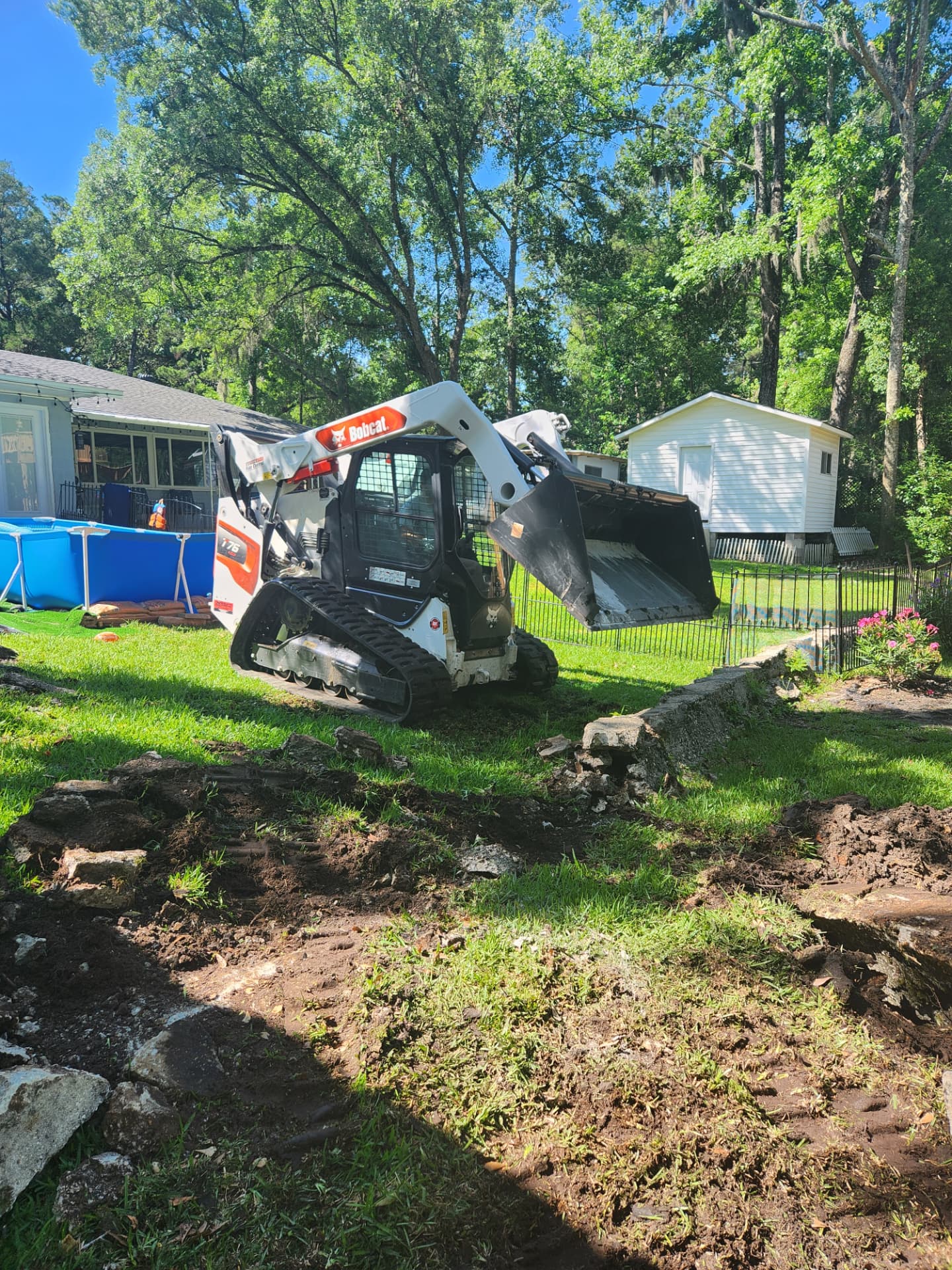 Track loader grading a backyard near a pool and fence
