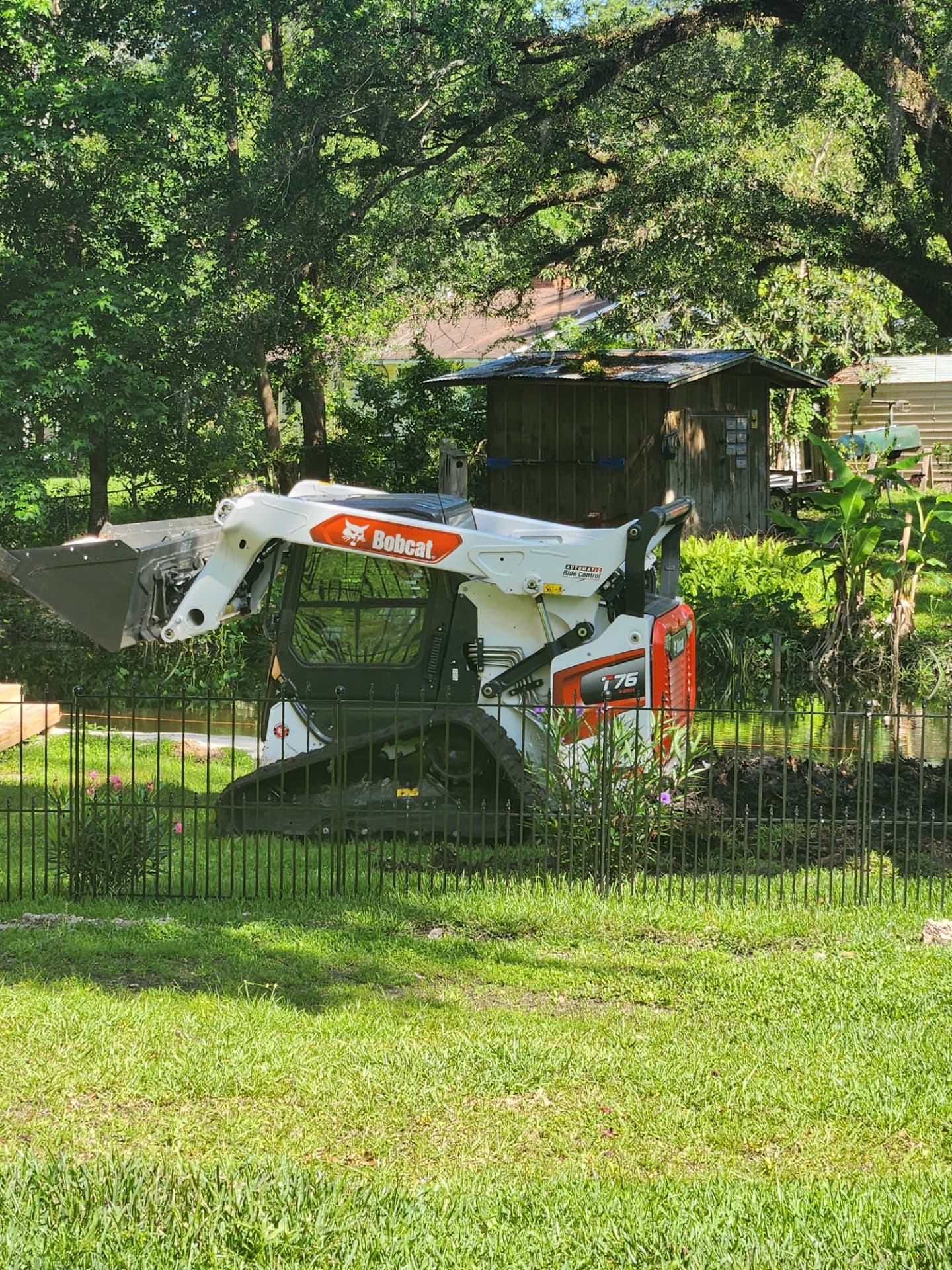 Bobcat loader parked on a lawn behind a fence, ready for brush work